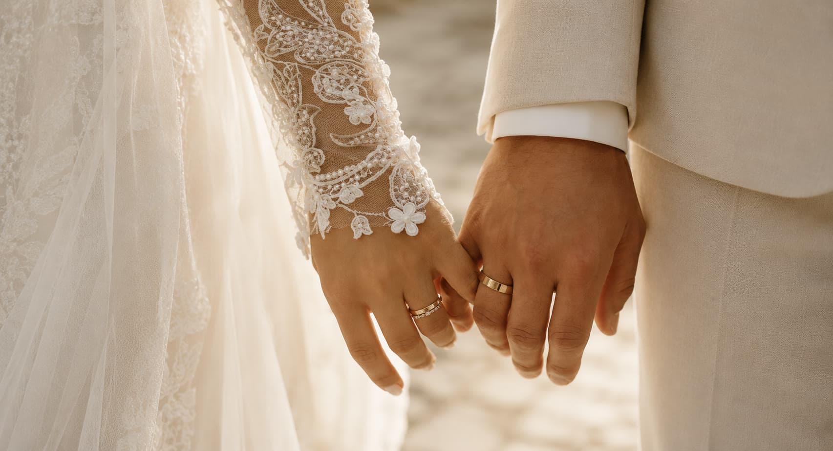 A bride and groom holding hands, both wearing their gold wedding bands