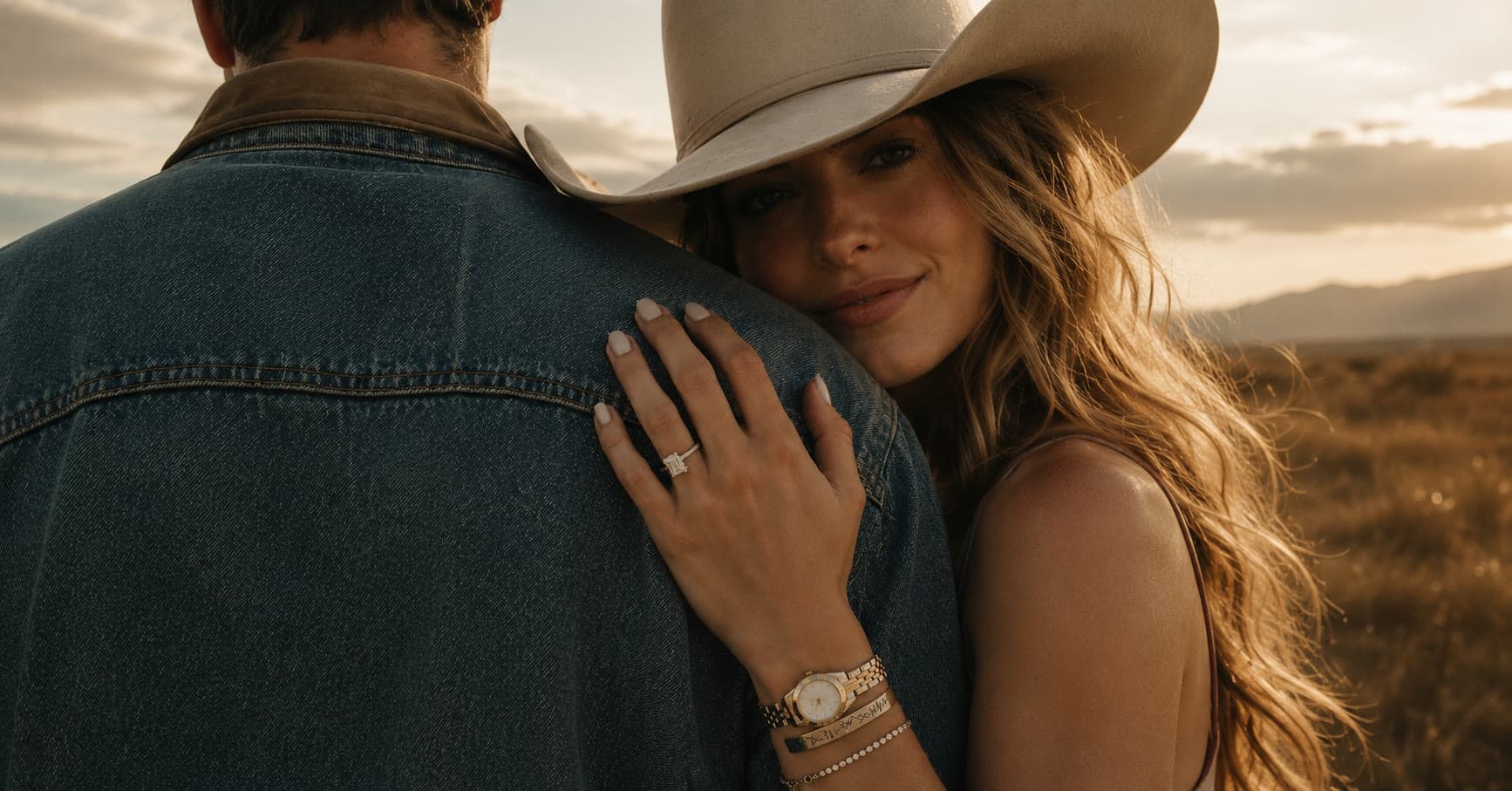 A couple at golden hour, her engagement ring resting on his shoulder